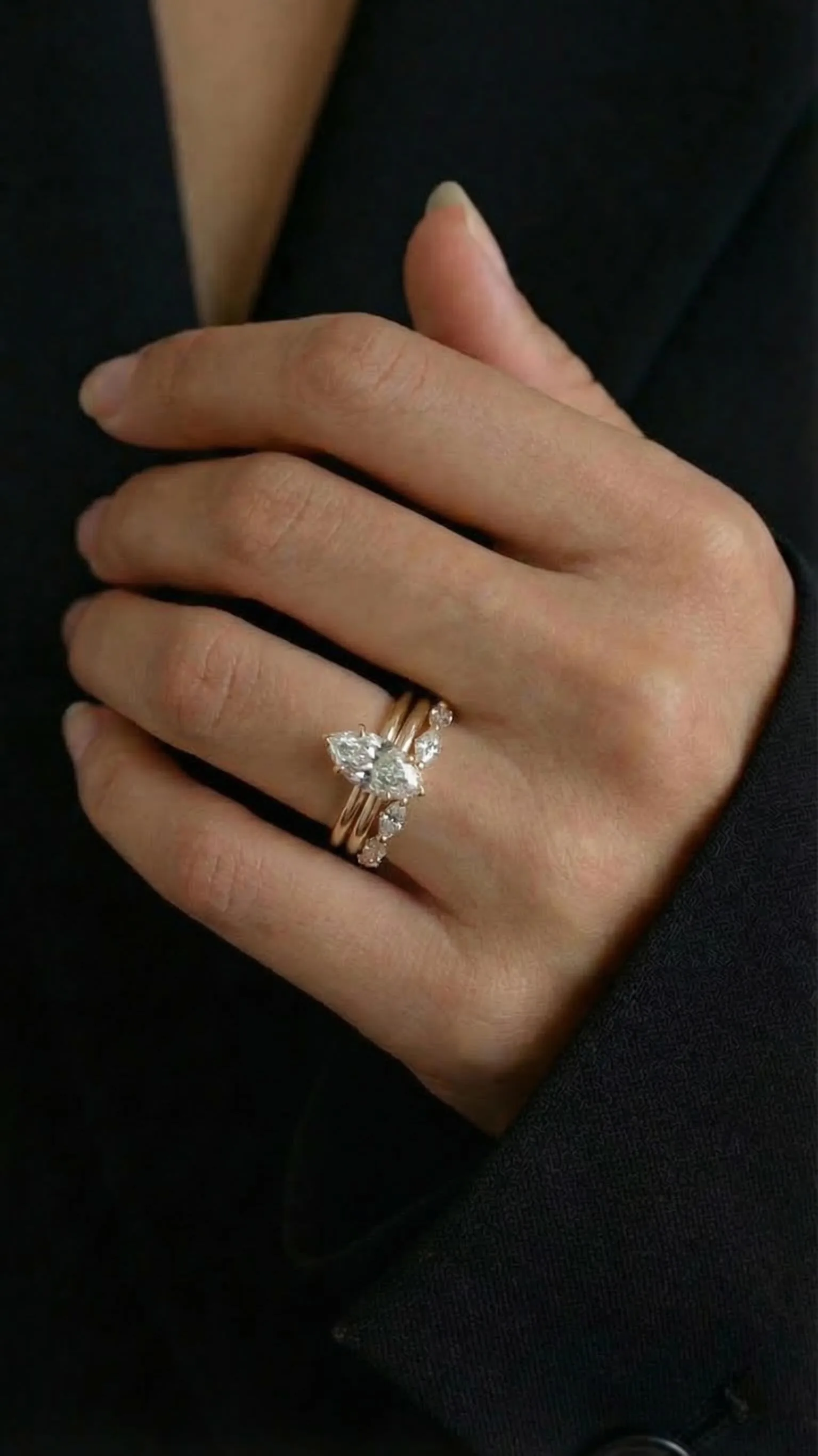 Marquise diamond solitaire engagement ring in yellow gold, stacked with a plain gold band and a marquise diamond wedding band, worn against a black blazer, by Lily Dia Jewellery