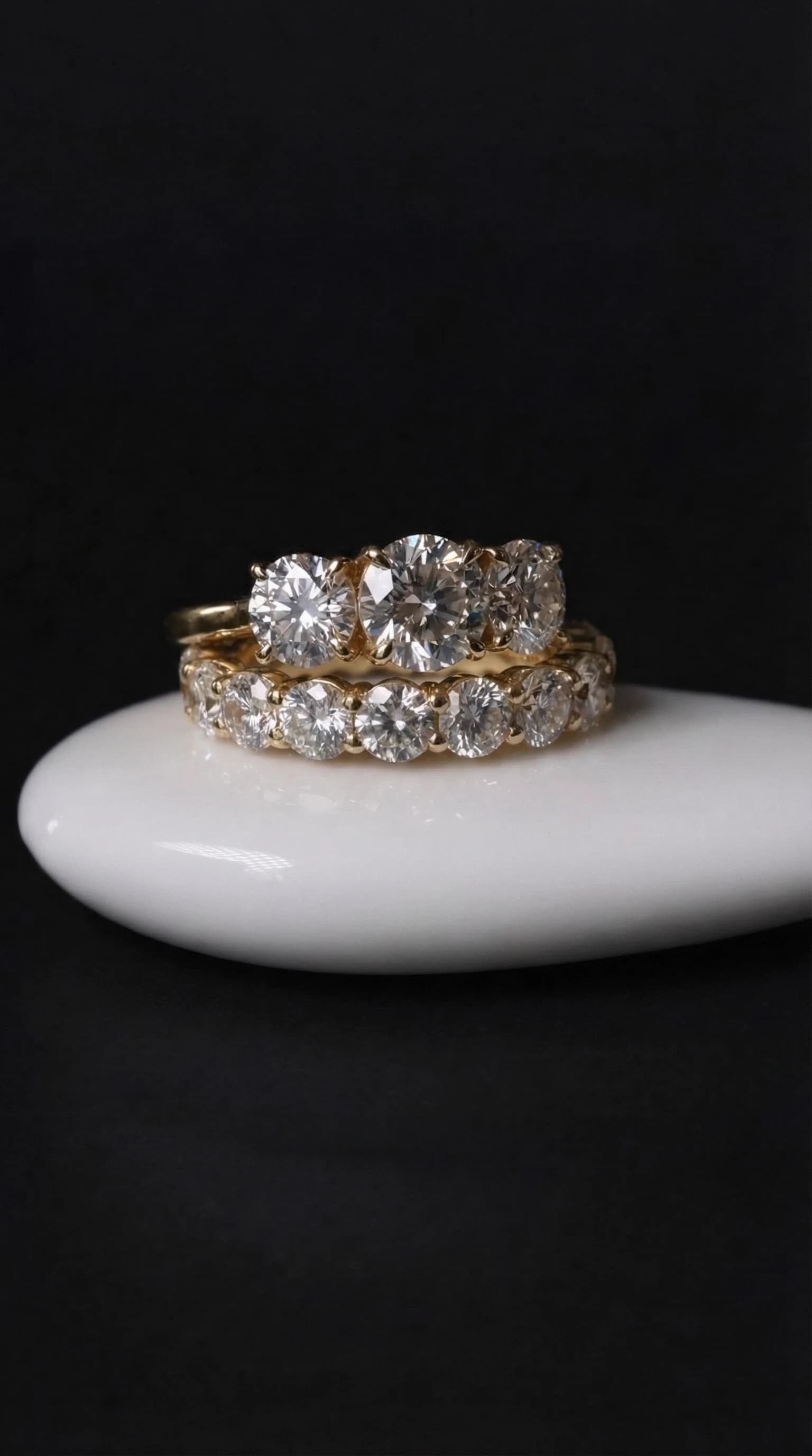Round three-stone diamond engagement ring stacked on a round diamond eternity band in yellow gold, by Lily Dia Jewellery
