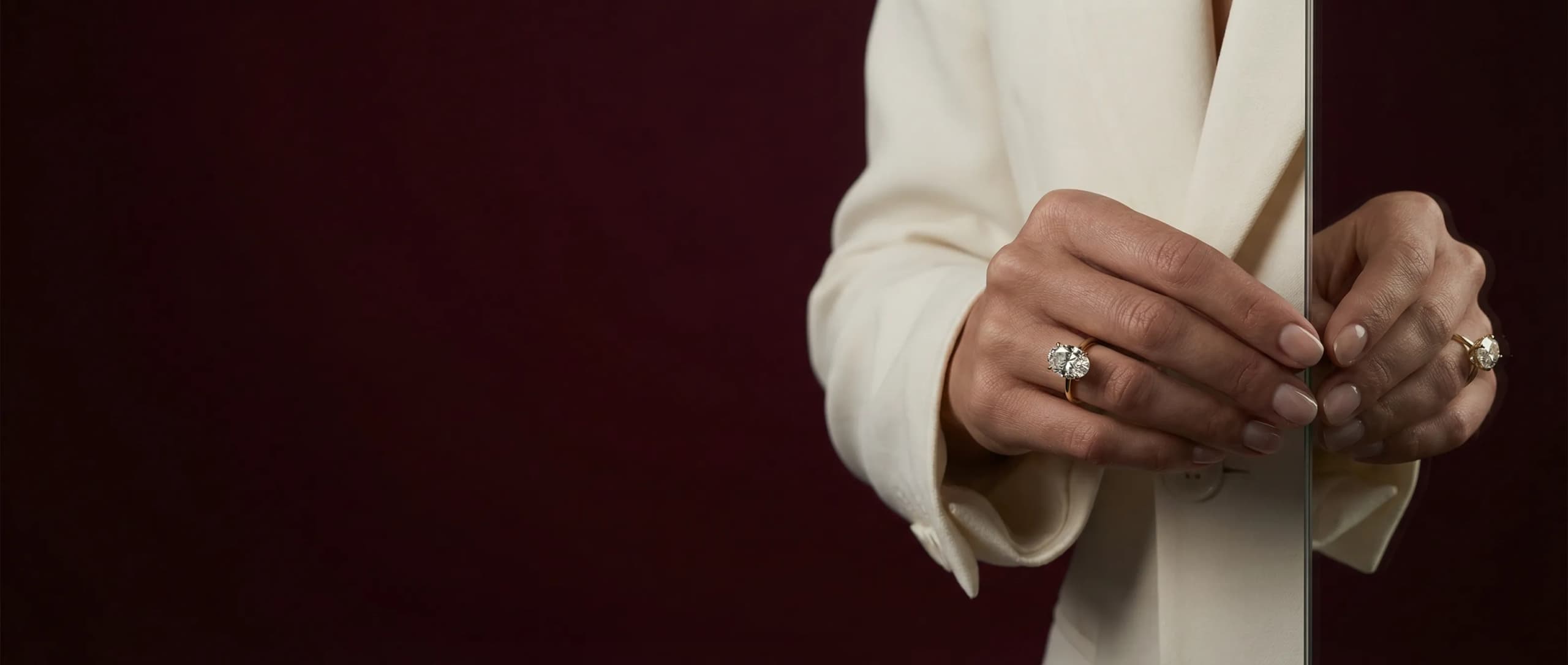 Oval lab-grown diamond solitaire engagement ring in yellow gold, worn with a cream blazer, by Lily Dia Jewellery