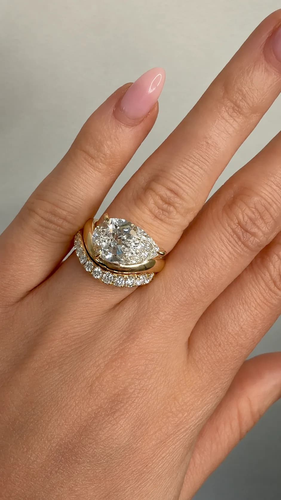 East-west pear lab-grown diamond engagement ring in yellow gold, worn with a curved pavé wedding band, by Lily Dia Jewellery